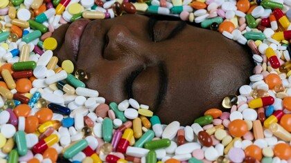 A woman's face is surrounded by scattered multivitamins, symbolizing the overwhelming presence of supplements in daily health routines
