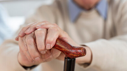 An elderly man's hands gripping a walking stick for support
