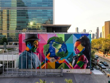 "Mural Nações Unidas", de Eduardo Kobra, em Nova York. A composição mostra um pai entregando o planeta à filha, cercados pelas cores e formas geométricas características do artista. A obra amplia a presença de Kobra no cenário internacional ao transformar a arte urbana em uma reflexão sobre responsabilidade ambiental e o futuro das próximas gerações
