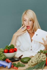 Woman holding a tablet and making a surprised face while looking at a table full of vegetables