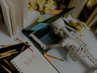 A skeleton slumped over a laptop, surrounded by crumpled papers and scattered notes, symbolizes the law of disintegration, where an excessive workload drains an individual until nothing remains but exhaustion