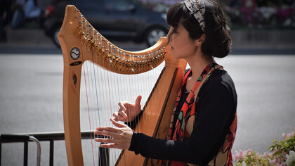 A beautiful Japanese woman in a black long-sleeve shirt playing the harp on a street in Kyoto, Japan