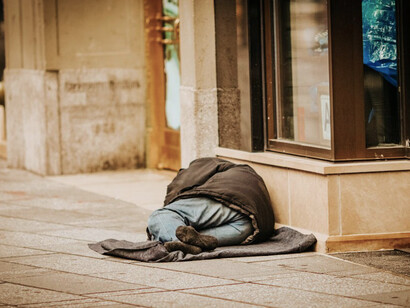 A homeless man resting on the pavement in an urban area
