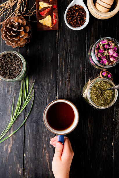 A top view of various dried spices and herbs, including black tea leaves, peppermint, rose, and Ayurvedic herbs