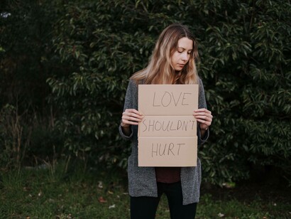A woman looking for answers as she holds up a sign of "love shouldn't hurt"