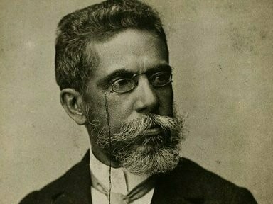 Machado de Assis com 57 anos. Em Teatro e Verdade, publicada na Gazeta de Notícias em 1885, Machado ironiza a obsessão da elite carioca pelas óperas italianas: "Aplaudimos com fervor o que não compreendemos, e compreendemos com entusiasmo o que não conseguimos sentir". O contexto era revelador: enquanto Carlos Gomes conquistava reconhecimento na Europa com O Guarany (1870), o público carioca preferia as companhias europeias itinerantes, que traziam repertórios muitas vezes desconexos com a realidade local
