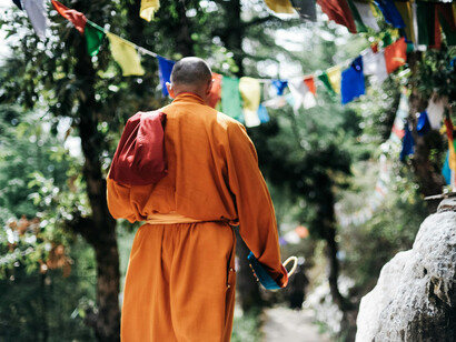 An unrecognizable Buddhist monk walking through a lush green garden in Lumbini, Nepal, surrounded by trees and sunlight filtering through the leaves