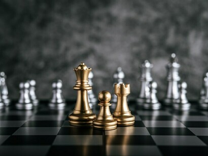 Gold and silver chess pieces on a chessboard, symbolizing a battle of strategy and reflection