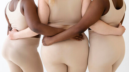Three women stand together, arms intertwined, their bodies visible rejecting narrow ideals