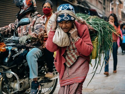 A woman carrying crops down a busy street