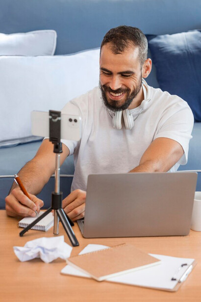 A content creator at home, multitasking between vlogging and managing social media on his laptop