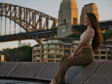 A woman stands near the Sydney Harbour Bridge during sunset in New South Wales, Australia