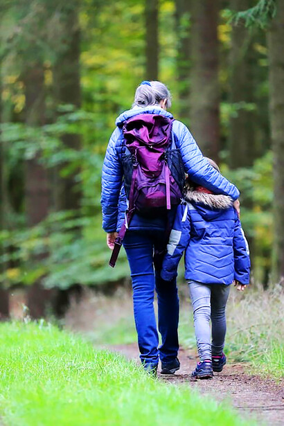 Amidst the picturesque scenery, a confident woman donning blue denim jeans and a black jacket is gracefully walking alongside her daughter
