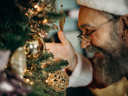 Avô vestido de papai noel termina decoração da árvore de natal
