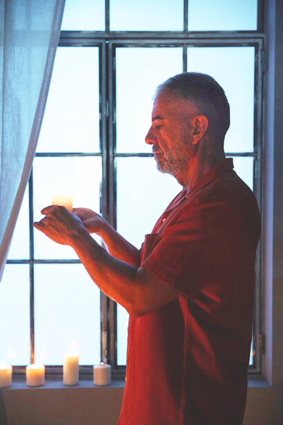 An elderly man holding a candle in prayer, embodying the spiritual struggle and journey of redemption and renewal through faith and scripture