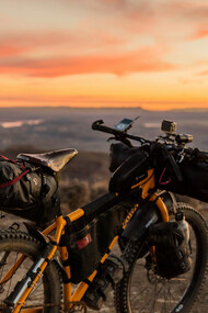 An orange and black off-road bicycle perched on a hill during sunset, with the warm glow of the fading light illuminating the scene