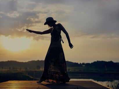 A woman standing at the edge of a pier is dialoguing with nature during sunset in a form of dance