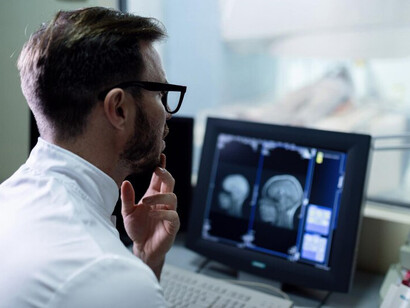 A radiologist reviewing a patient's brain MRI scan on a computer monitor in the control room