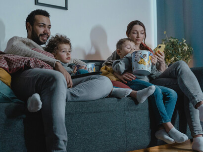 A man and a woman sit on a blue sofa, eating popcorn together as a family