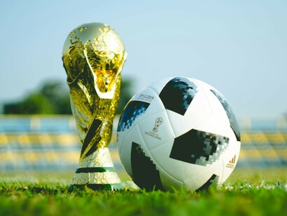 A gold-colored trophy resting on the grass field during the daytime, accompanied by a football