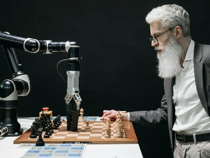 A man engaged in a chess match with a humanoid robot, symbolising the evolving contest between human intellect and artificial intelligence