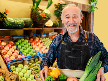 Local grocery store owner organizing fresh fruits and vegetables in a produce box, highlighting the appeal of small independent shops