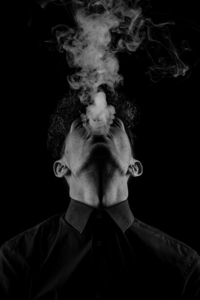 A person dressed in a black long-sleeve shirt smokes in the distance