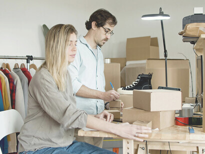 A man and a woman work together to pack products at a table in a small warehouse
