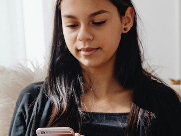 Using her mobile phone, a woman in a black long-sleeved outfit binge-watches short vertical drama episodes designed for smartphone viewin