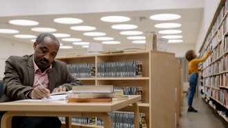 Pessoas em uma biblioteca estudando e escolhendo livros de teoria literária