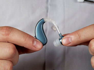 A doctor carefully holding a modern hearing aid between their fingers, representing the integration of connected medical devices with the human body