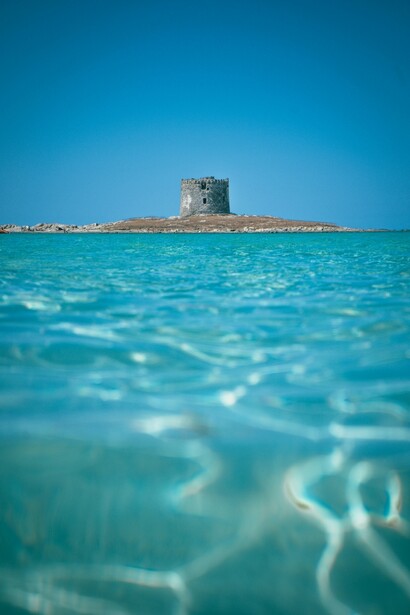 La Spiaggia La Pelosa, situata vicino a Stintino, in Sardegna, è famosa per la sua sabbia bianca finissima e le acque turchesi cristalline che ricordano i Caraibi. La vista sulla Torre della Pelosa, una torre aragonese del XVI secolo, aggiunge fascino a questo luogo suggestivo