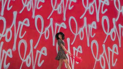 A woman standing in front of a "love" graffiti that serves as a reminder that self-love is everywhere you go no matter the season or reason