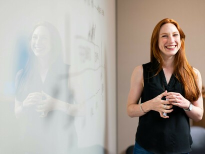 A female software engineering student in a blue tank top standing beside a white wall, engaging in a teacher-student interaction