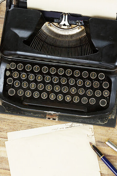 An old typewriter rests on a wooden desk, surrounded by historical diaries and literary archives