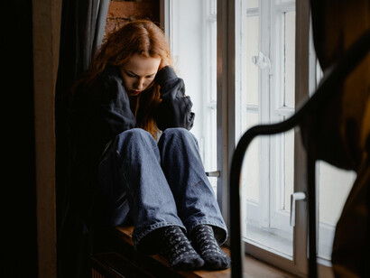 A woman sitting on a windowsill, wrapped entirely in her own isolation