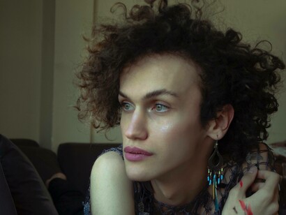 A trans woman who is part of the LBGTQ+ community is sitting in her living room and thinking about what to do next in her