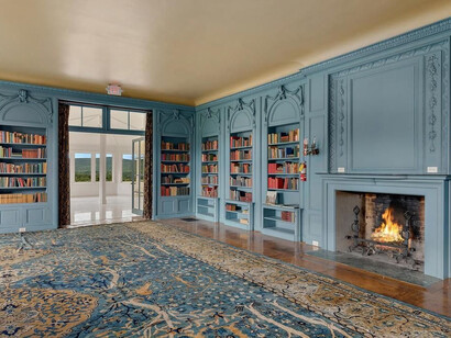 A notable timber-clad library with striking blue panelled walls, built-in bookcases, and a large fireplace. Photo by © Tricia McCormack