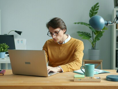 Um homem trabalha diante do laptop em uma mesa, em um espaço dedicado ao estudo ou ao trabalho. Isolado diante da tela, o indivíduo aparece integrado à lógica de concentração e produtividade que marca a sociedade do desempenho. Na sociedade do desempenho, estar permanentemente ocupado pode se tornar tão natural que a pausa, o ócio e até mesmo a percepção das próprias emoções parecem perder lugar