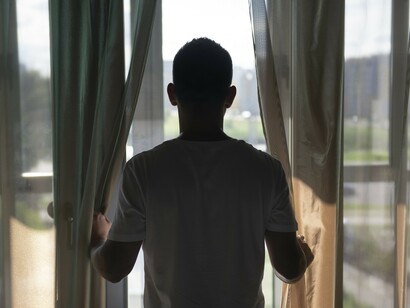 A man stands by the window in isolation, reflecting the quiet uncertainty and confinement of lockdown life