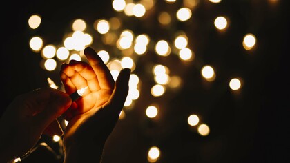A hand holding a small light against a backdrop of little lights, weaker than a single illuminating focus, but plural and decentralized