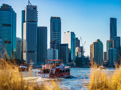 Sailboats resting on the Brisbane River beneath the city towers, reflecting the peaceful coexistence of urban life and the river