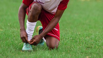 Jogador de futebol amarra a chuteira em campo