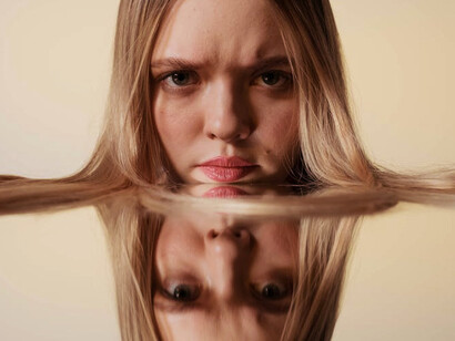 As the woman rests against the mirror, her face merges with her own reflection, blurring the lines between reality and illusion