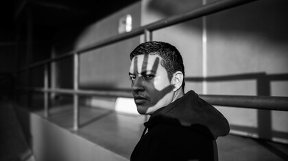 A monochrome photo of a man wearing a hoodie with the shadow of a hand on his face