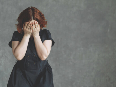 A woman rests against a concrete wall in visible distress, conveying the weight of stress and depression