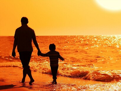 Un niño pasea de la mano de su padre junto al mar