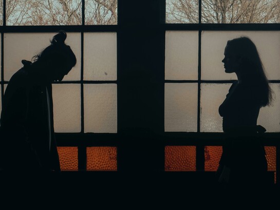 A man and woman standing in a dimly lit room, surrounded by darkness and emotional tension