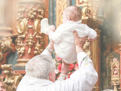A priest holding the baby high up in the church as he's about to begin to perform the baptism ceremony 