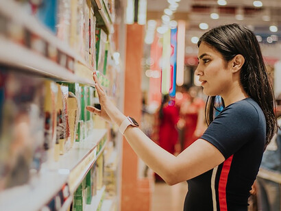 Amidst the bustling market, a woman stands engaged in shopping, her gaze focused on the shelves before her